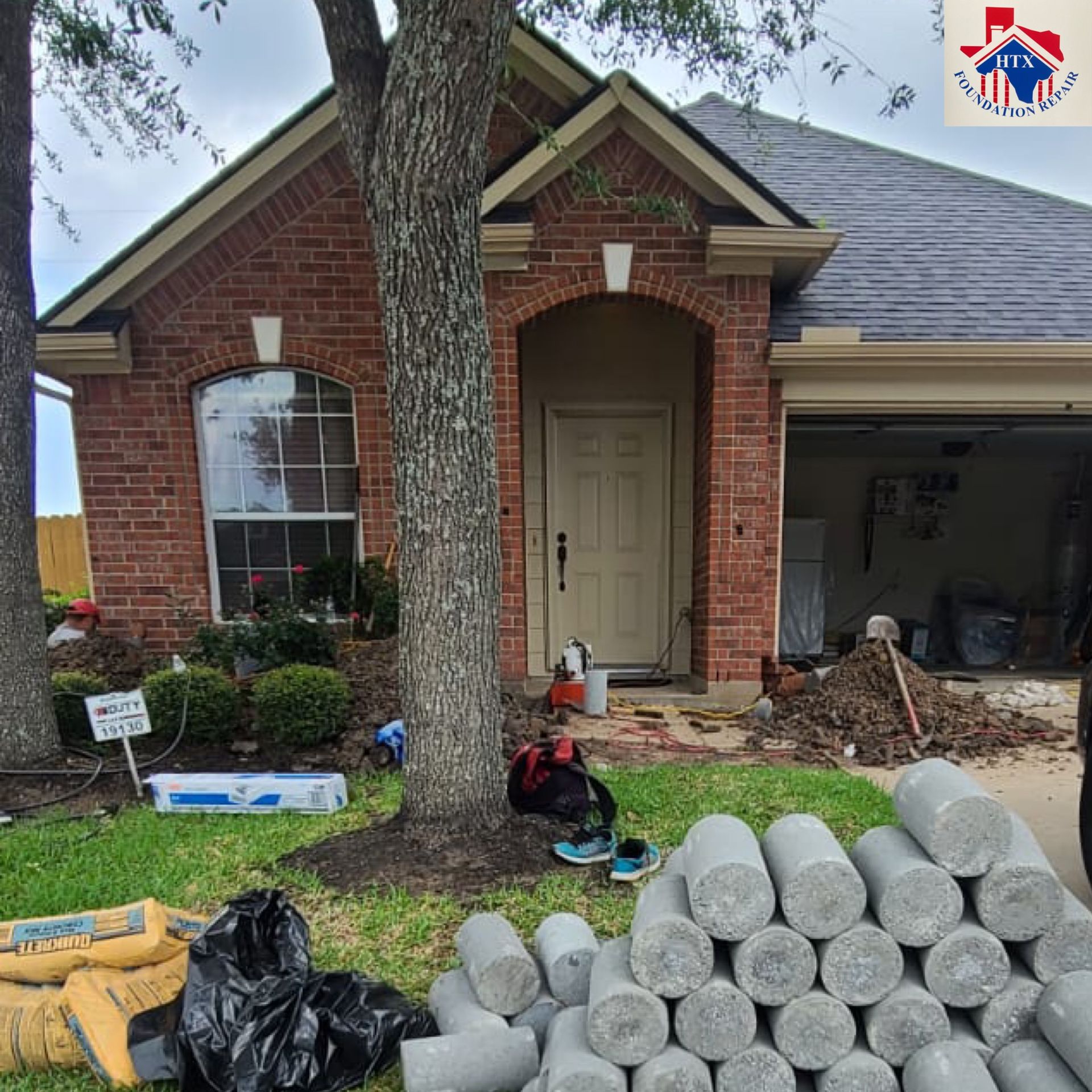 Front of a brick house with yard cluttered by rolled turf, trash bags, and construction debris.