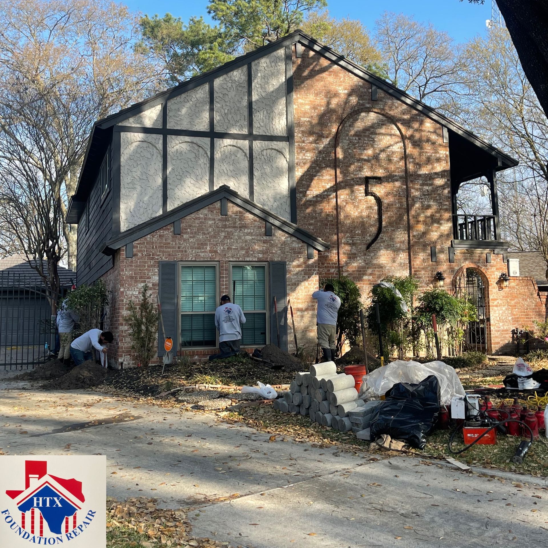 House exterior under renovation with workers, ladders, and construction materials in the front yard