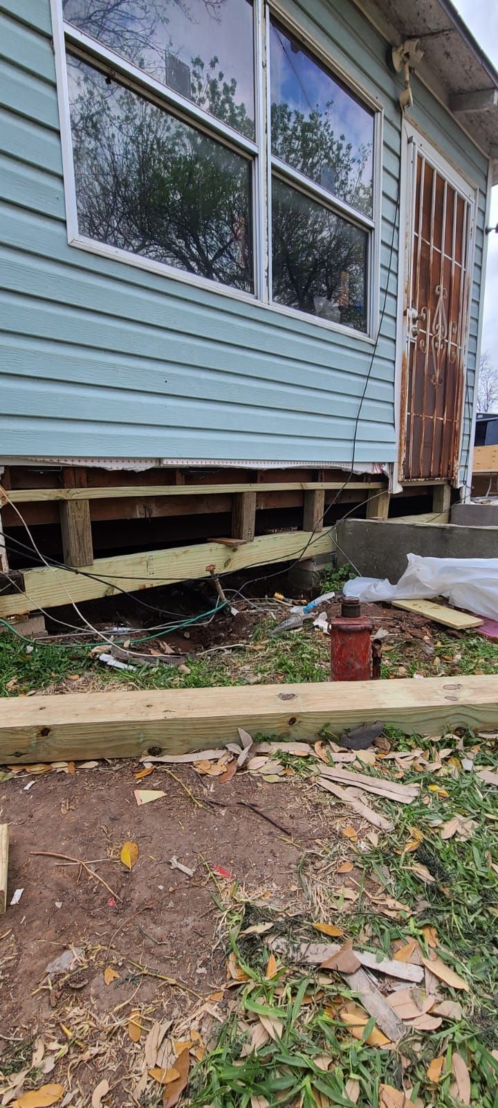 Partially collapsed porch on a house with exposed wooden framing and blue siding, beside a red planter and steps