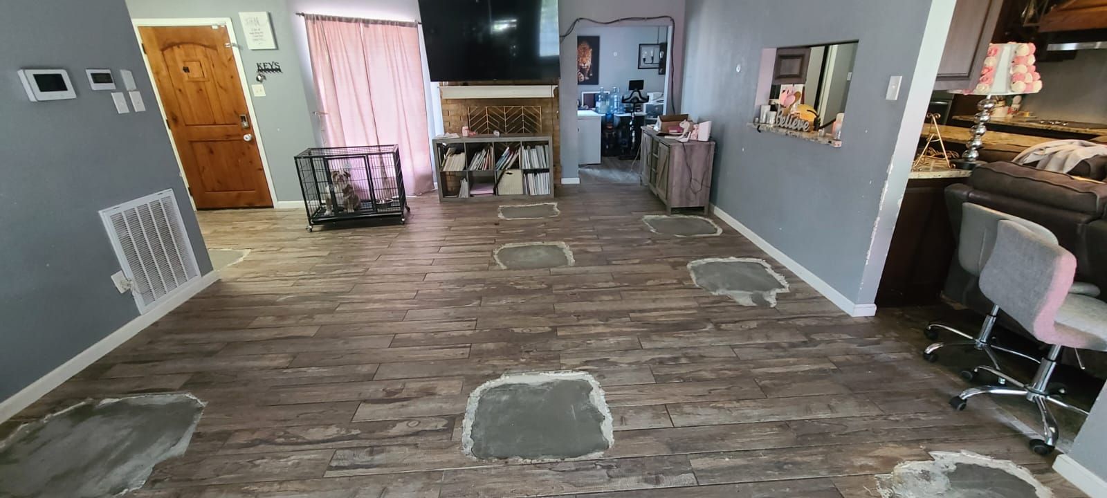 Empty living room with wood-look floor, gray walls, orange curtains, and scattered furniture.