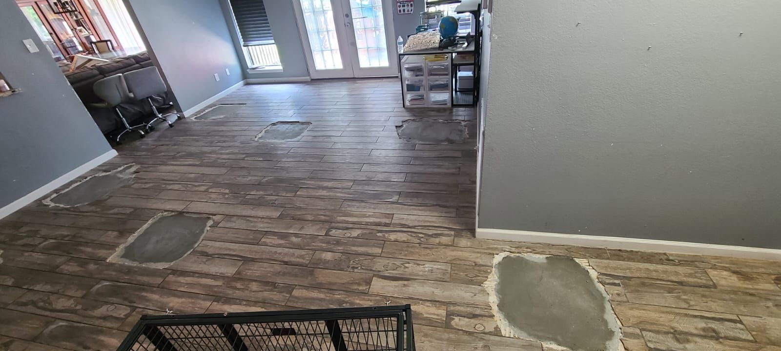 Hallway with worn tile floor, gray walls, and glass doors at the far end