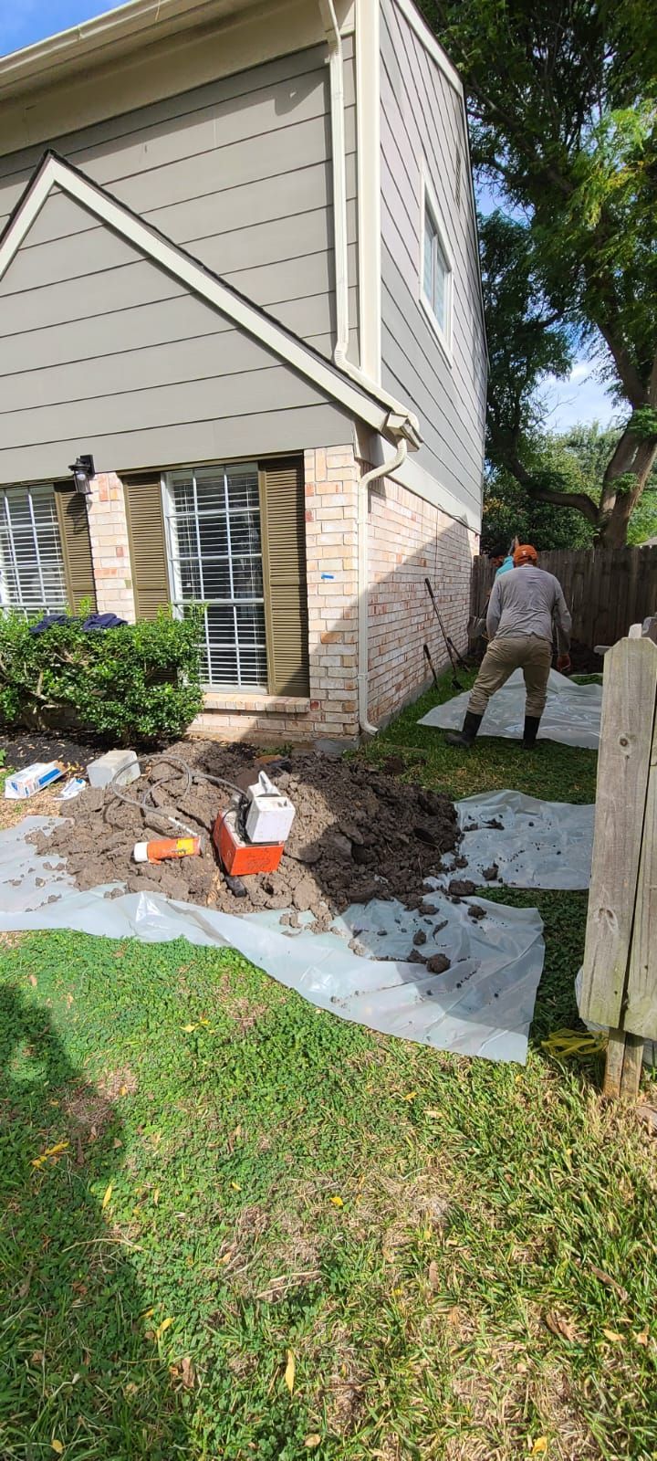 House exterior with a damaged brick wall and debris on a white tarp; person standing nearby in the yard