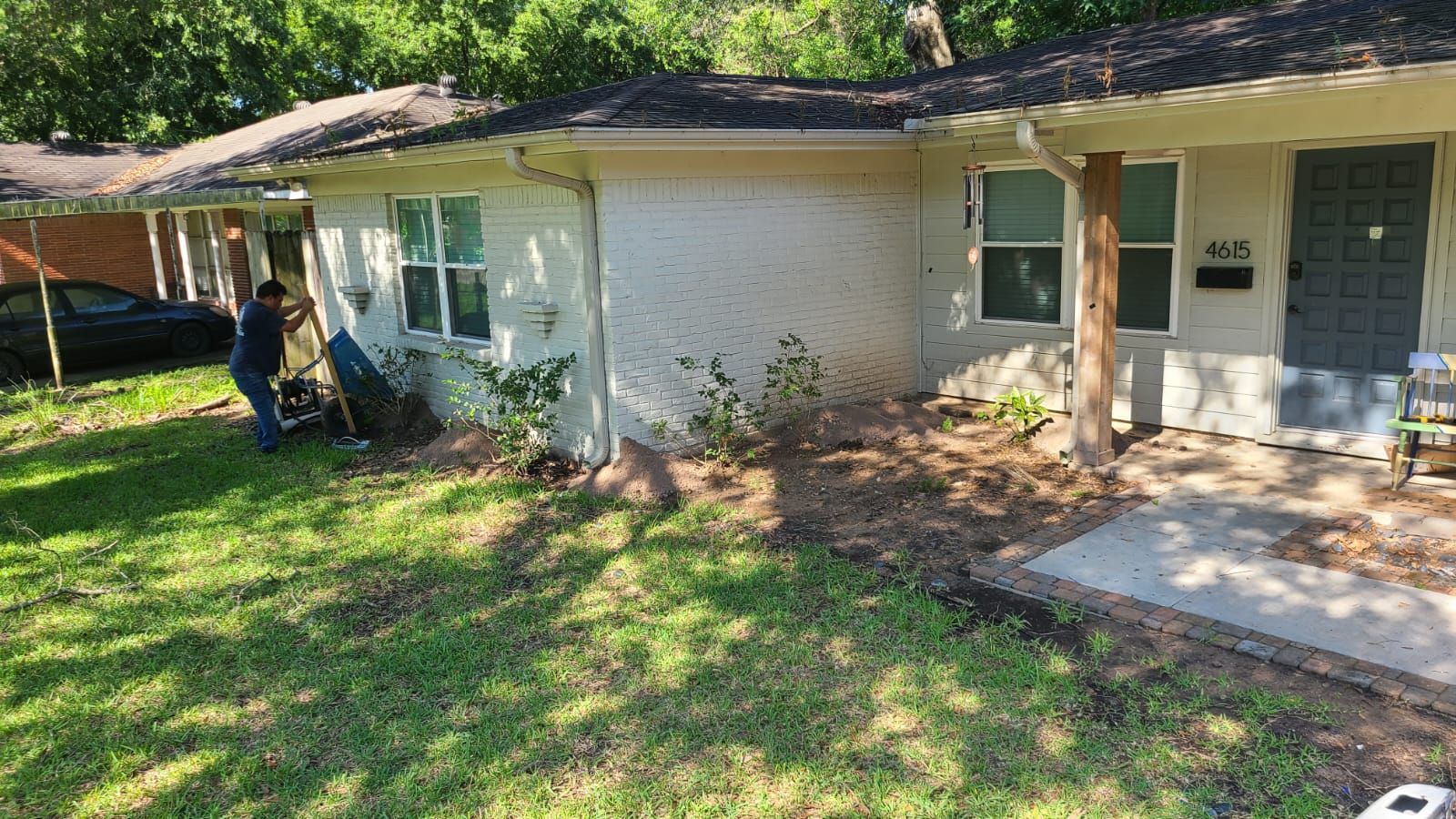 Single-story white house with front porch, blue door, and shaded lawn with trees and garden beds