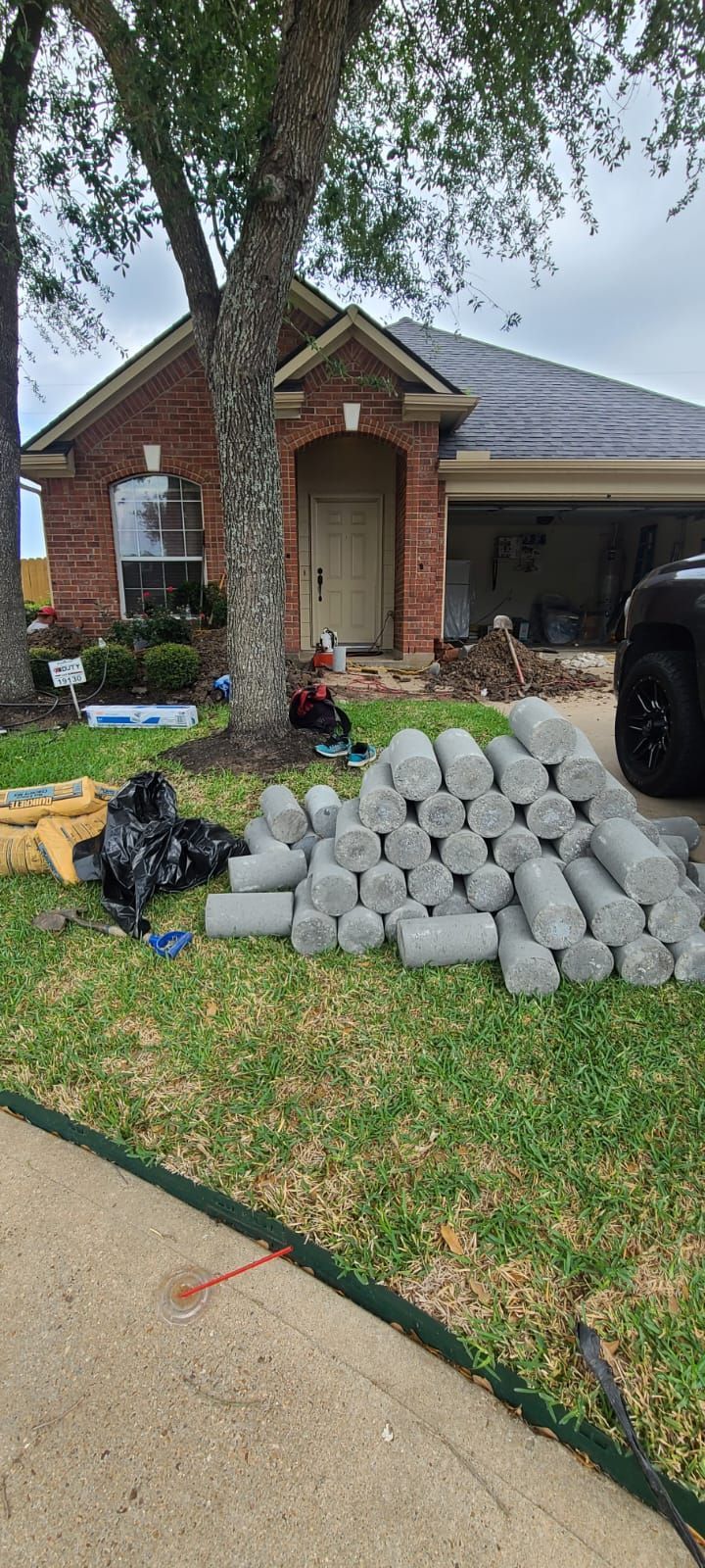 Front yard with stacked concrete pavers, a brick house, and a large tree near the driveway.