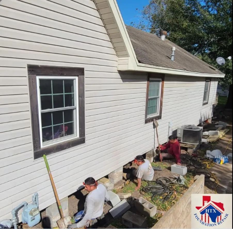 Workers repairing siding on a house exterior with tools and materials along the foundation