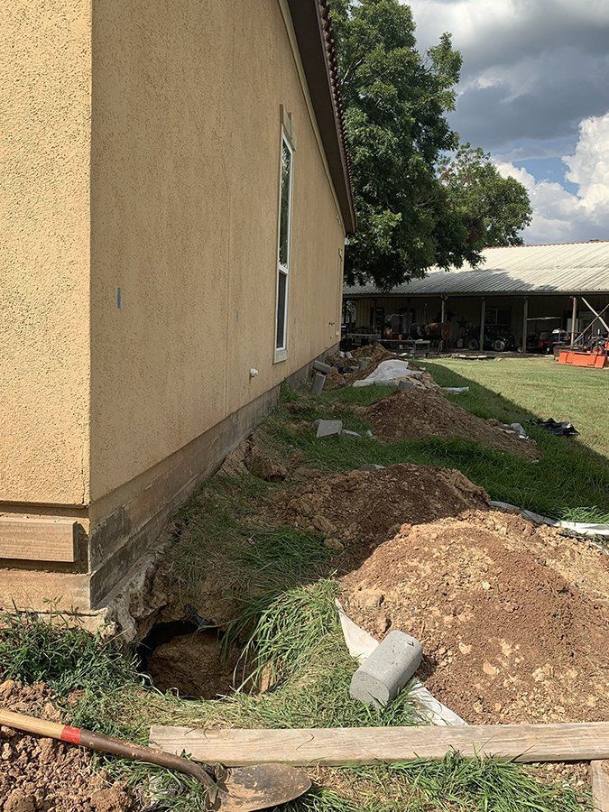 Side of tan building with a trench and dirt pile beside a grassy construction area