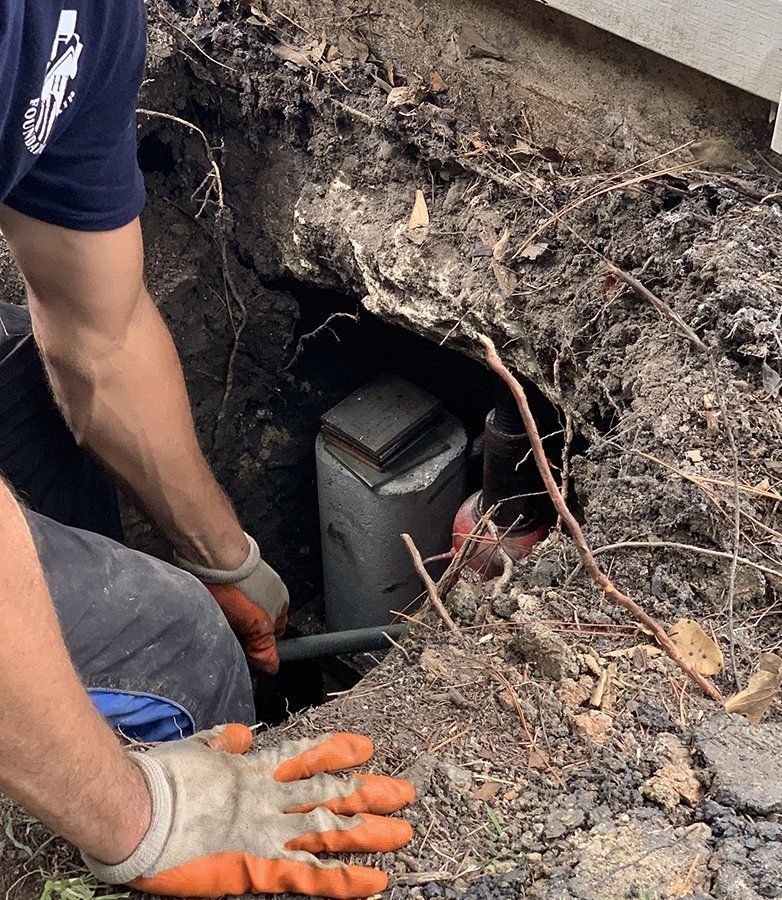 Worker in gloves kneels beside an exposed underground utility box in a dirt trench.