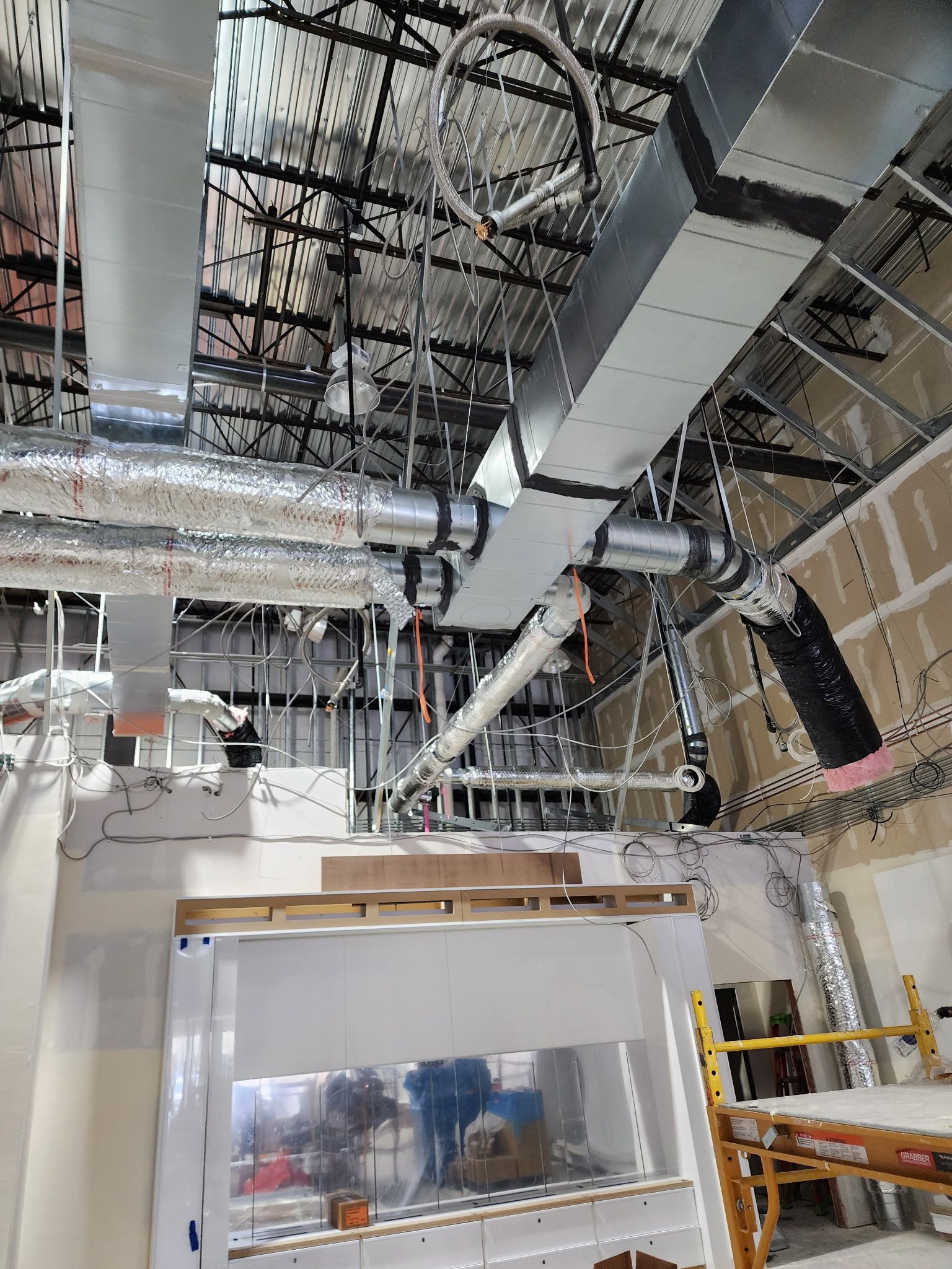 Construction site interior showing exposed metal HVAC ducts, wiring, and framing above a white service counter.