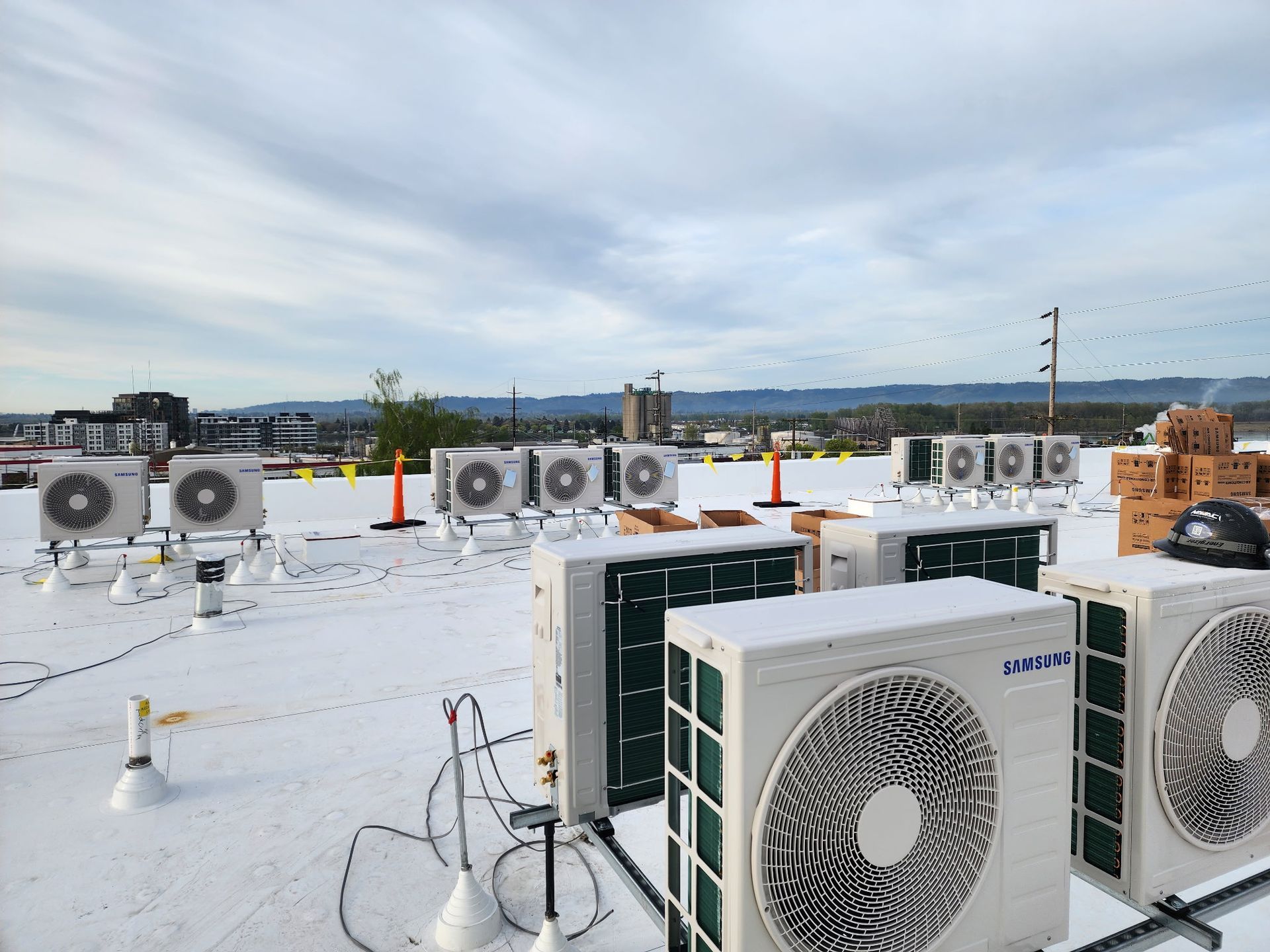 Multiple HVAC condenser units installed on a white flat roof against a background of distant mountains and a city skyline.