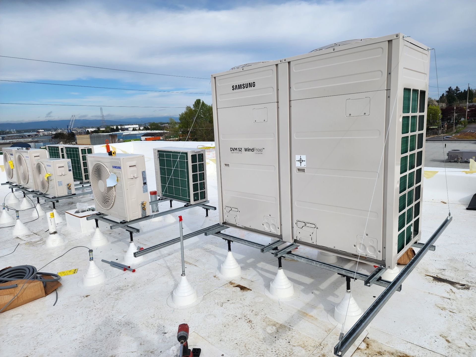 Rooftop HVAC units mounted on white support stands on a flat, light-colored roof under a blue, cloudy sky.