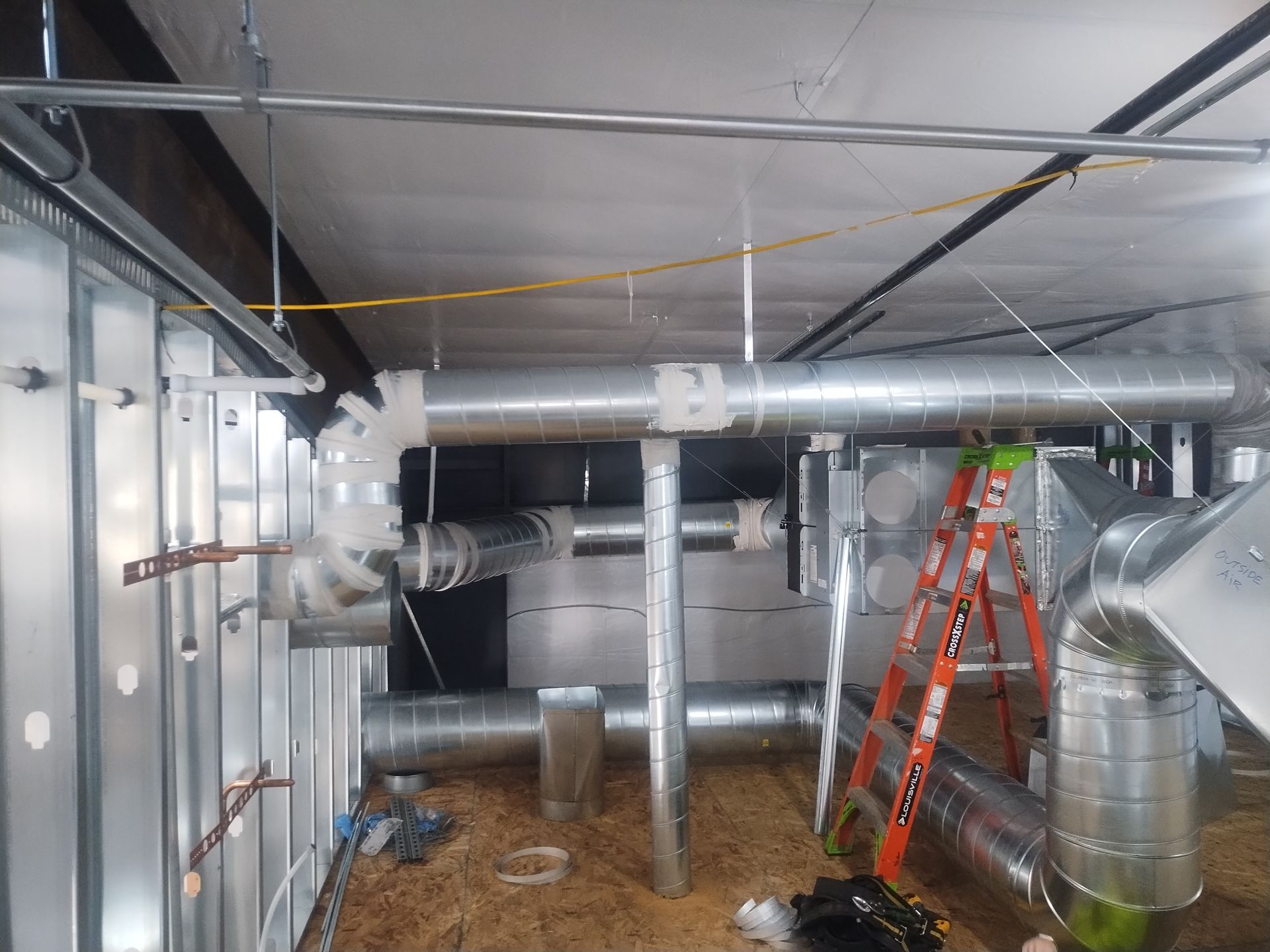 A room with a lot of pipes and a ladder in it