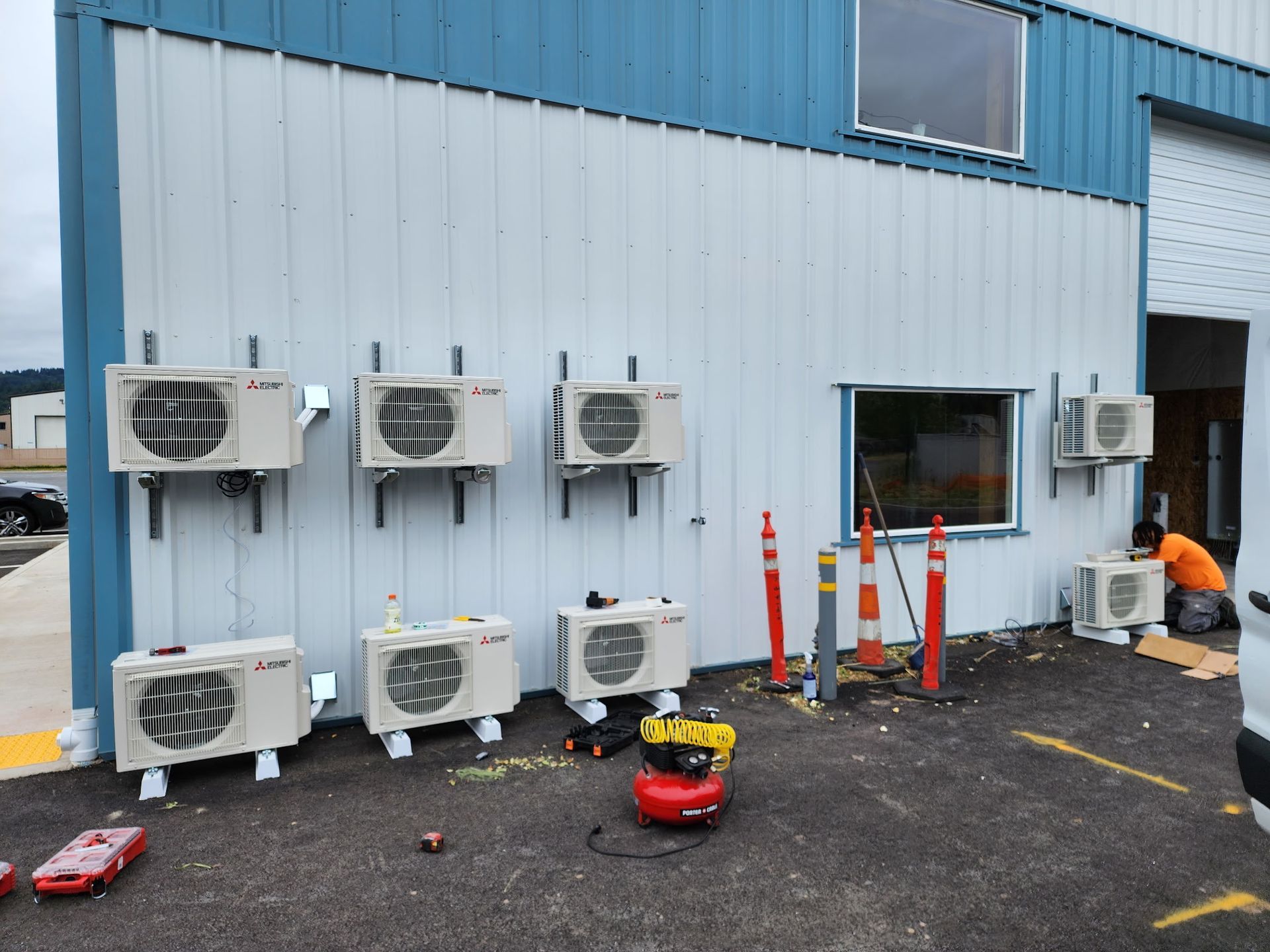 Several Mitsubishi air conditioning units mounted on building exterior; workers nearby.