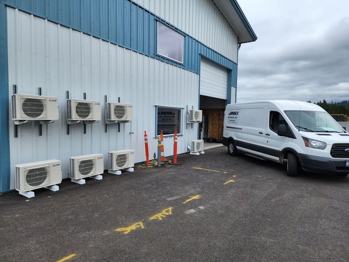 Air conditioning units mounted on a building exterior next to a white van parked on gravel.
