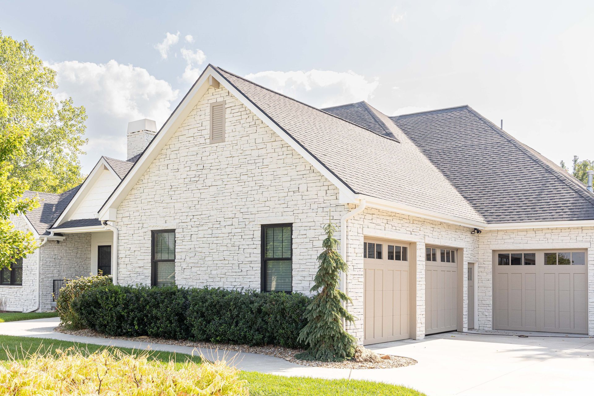 A white brick house with two garage doors and a gray roof.