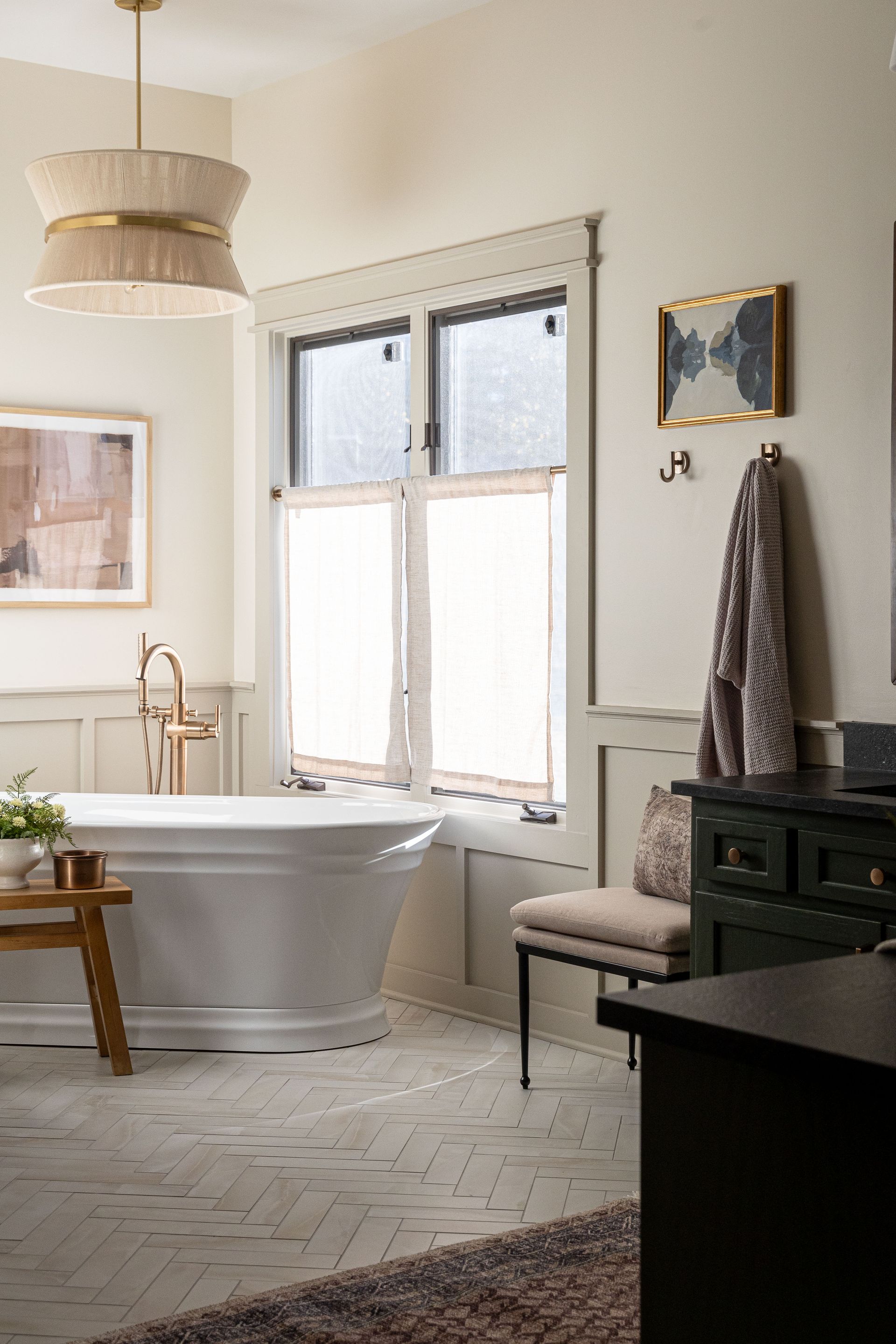 A bathroom with a tub , dresser , chair and window.