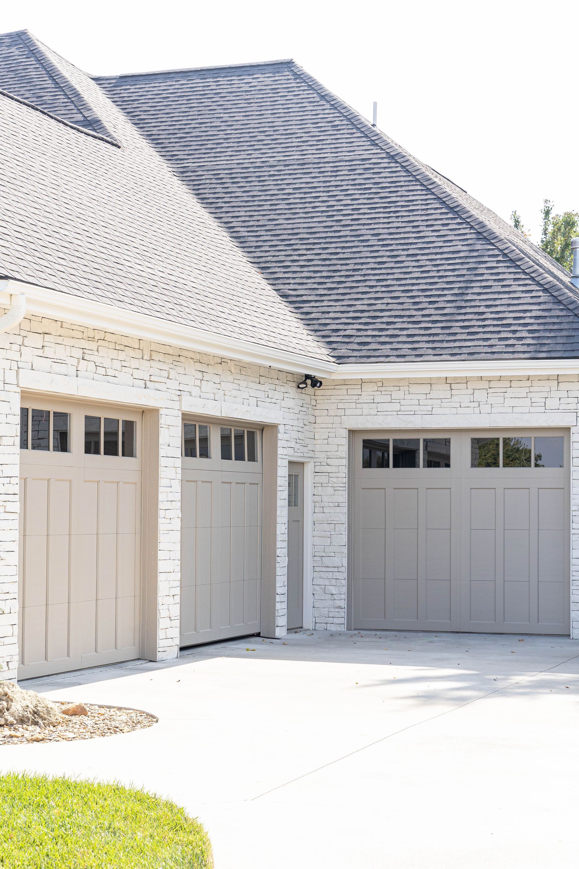 A white brick house with three garage doors and a black roof.