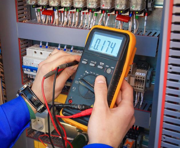 Technician measuring voltage in an electrical control panel with a digital multimeter