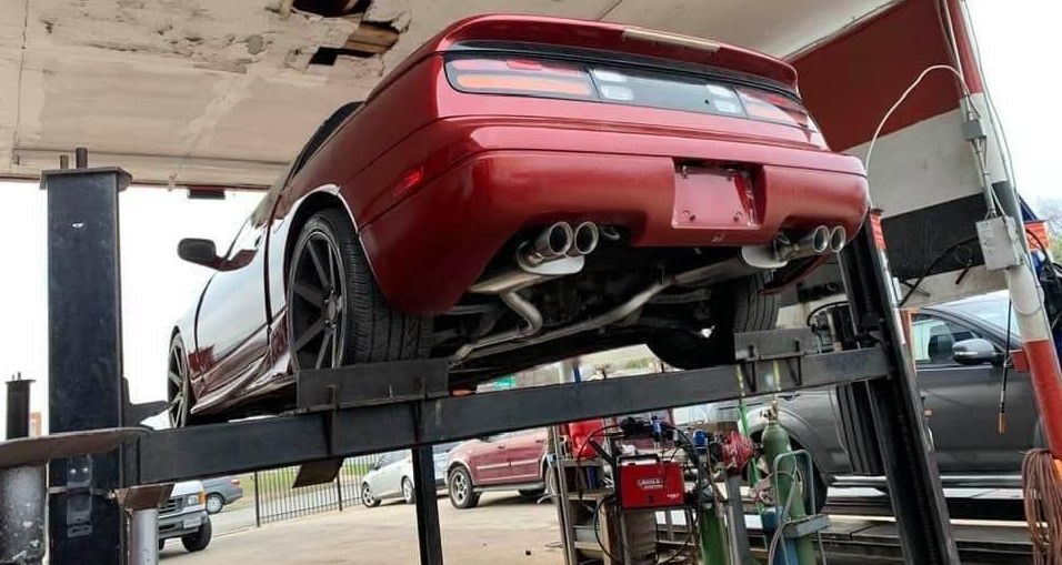A red car is sitting on a lift in a garage.
