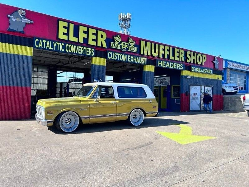 A yellow car is parked in front of a muffler shop.