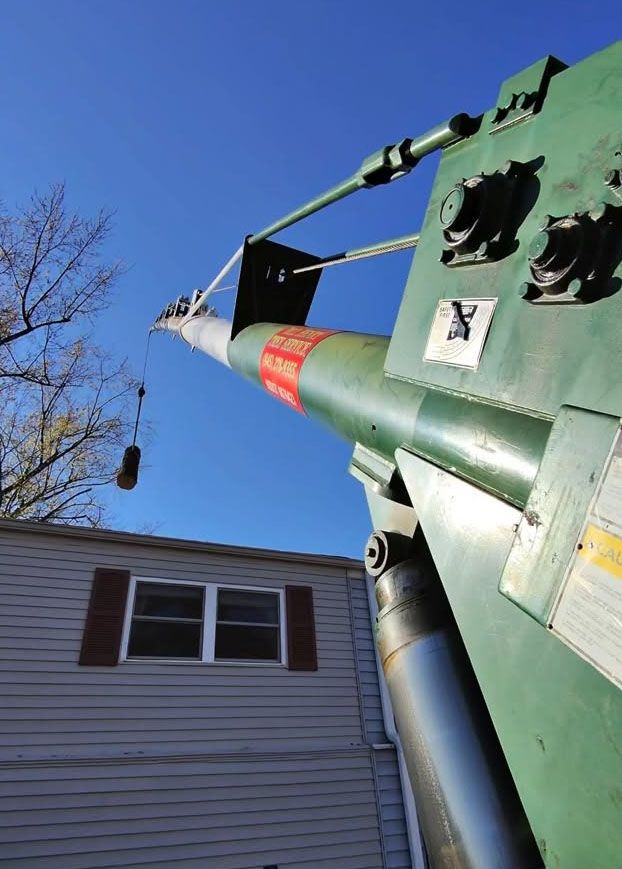 Green crane boom lifting over a house roof against a blue sky.