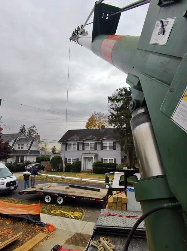 Crane lifting a long metal beam over a suburban street under cloudy skies.