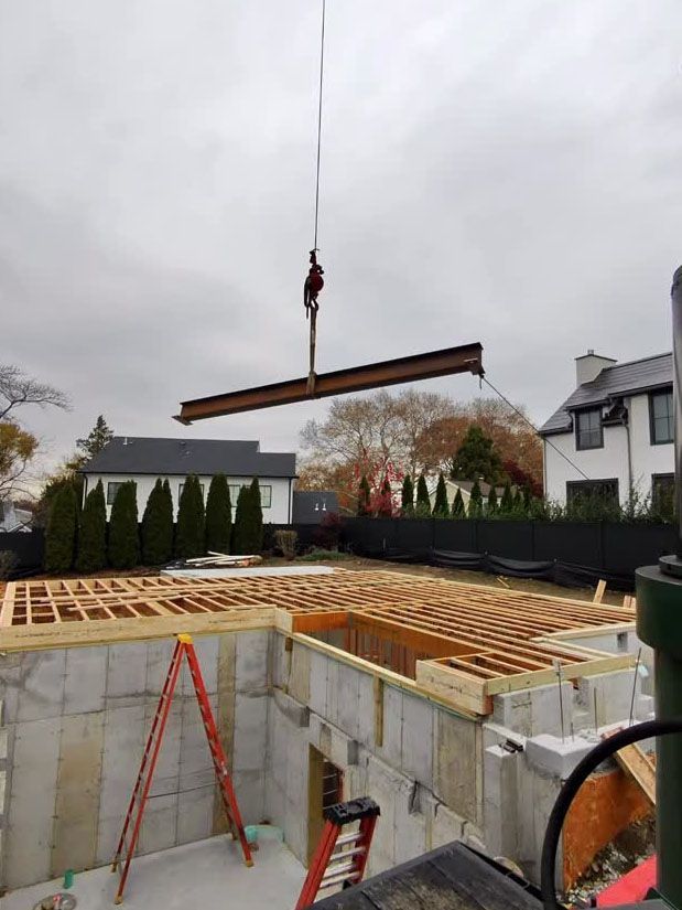 Crane lifting a long beam over a house under construction with exposed wooden framing.
