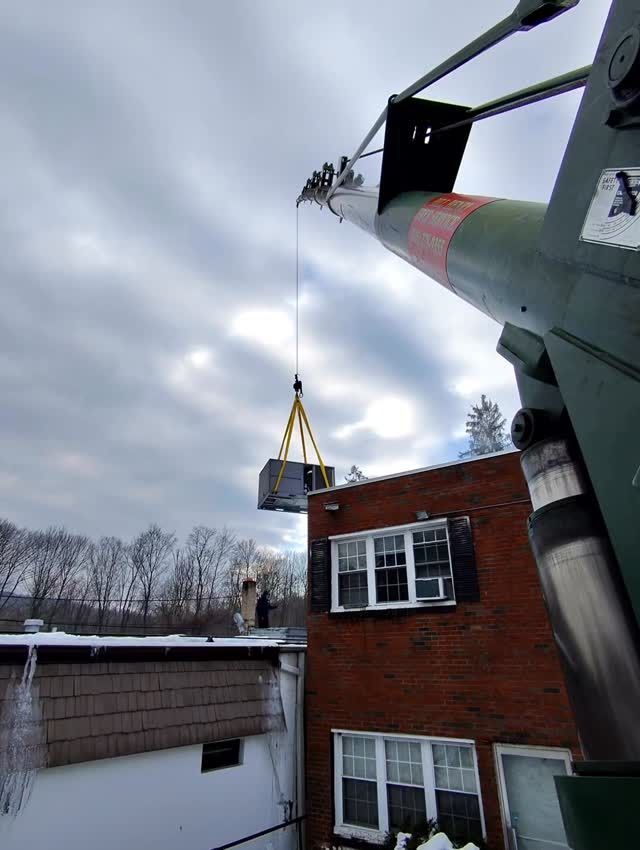 Crane lifting a large object over a brick building in winter under a cloudy sky.