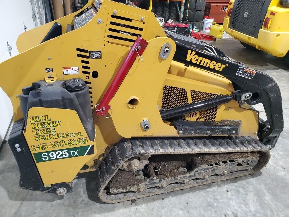 Yellow Vermeer S925TX tracked skid steer with black tracks and front attachment in a snowy yard