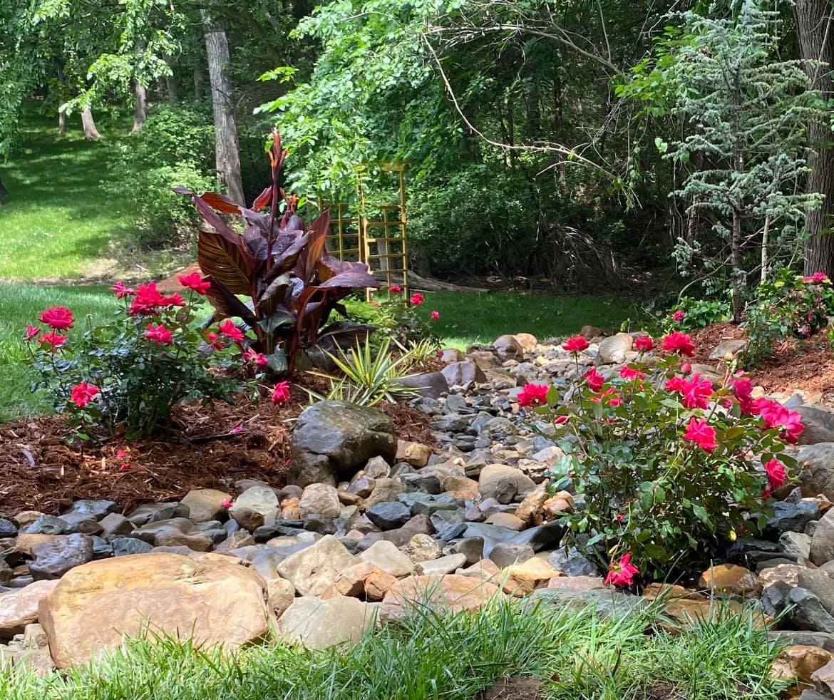 A garden filled with rocks and flowers with a stream running through it.