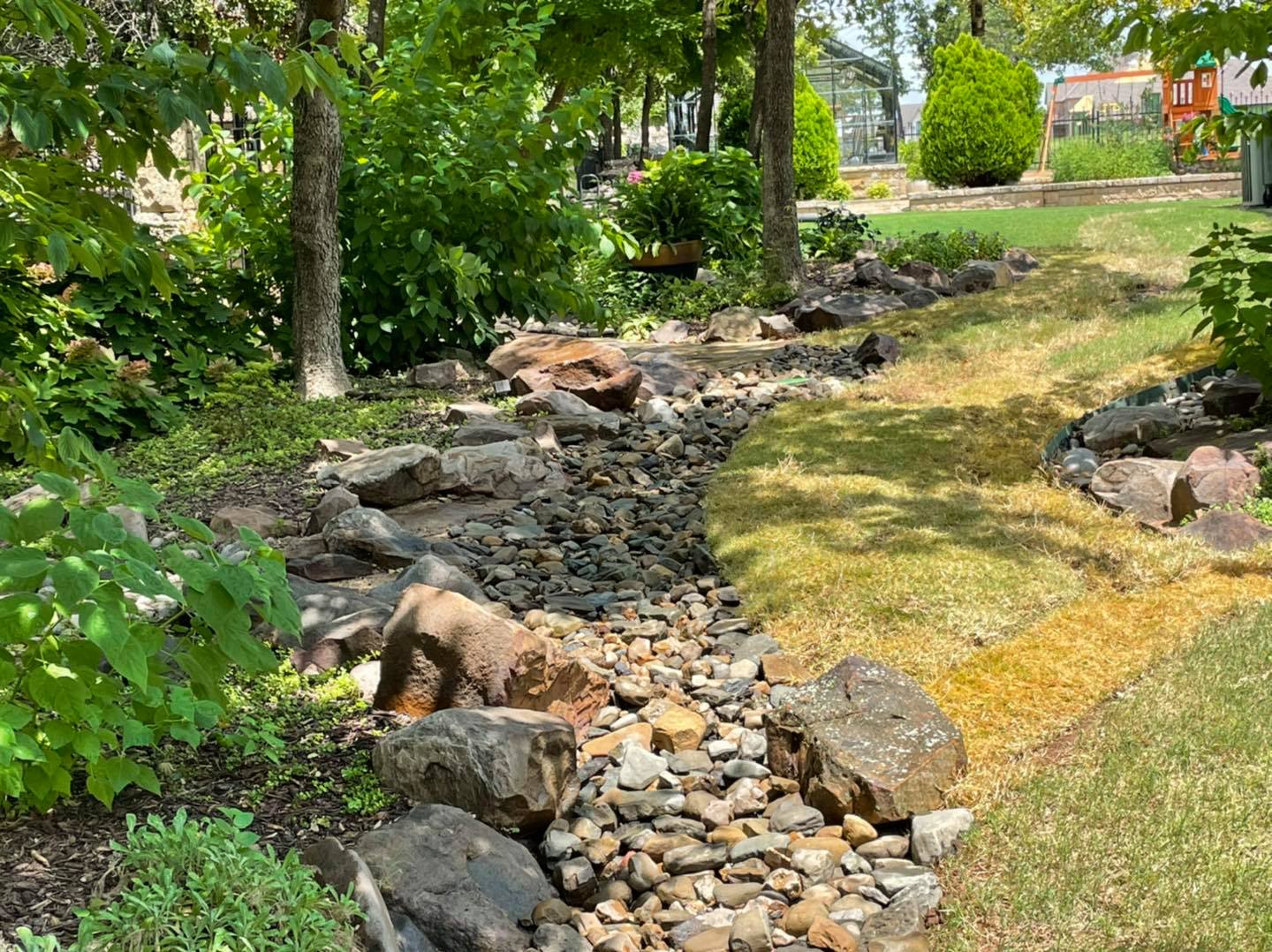A stream running through a park surrounded by rocks and trees.