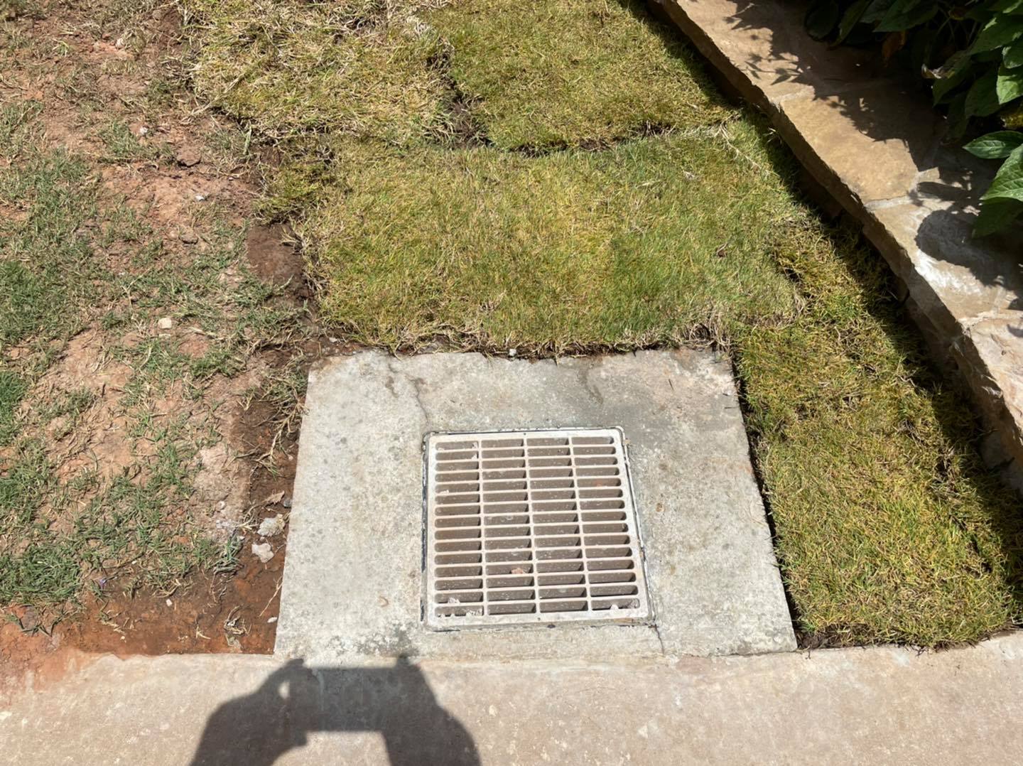 A manhole cover is sitting in the grass next to a sidewalk.