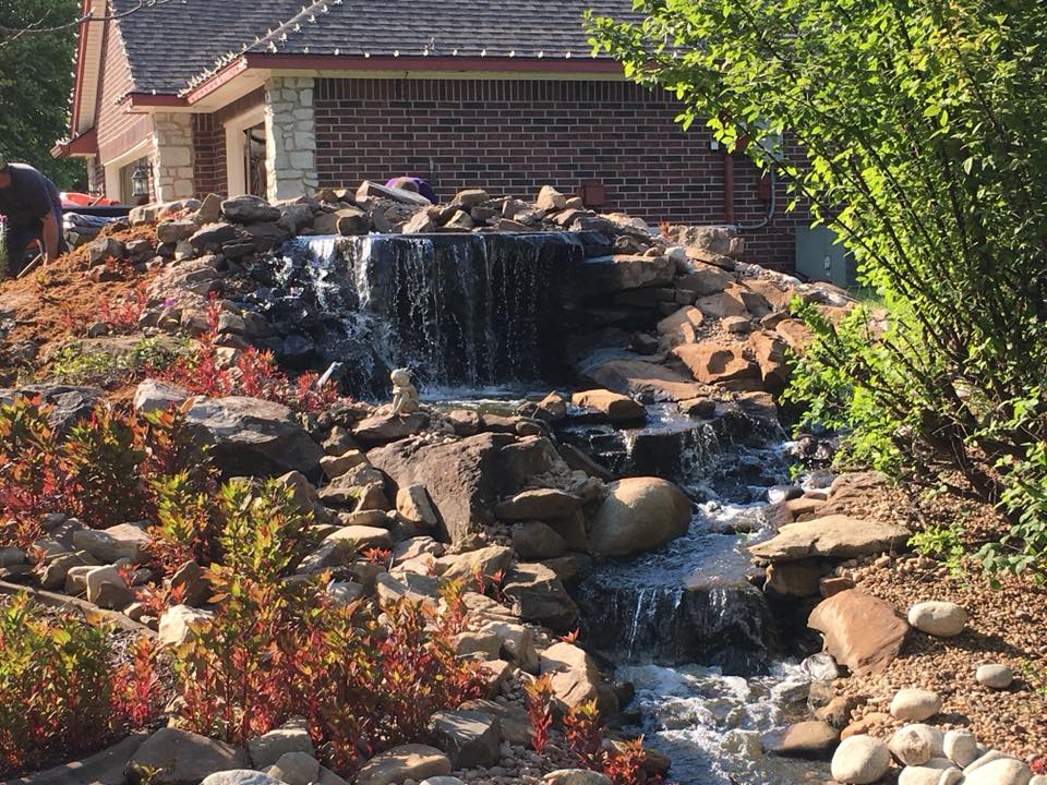 A waterfall is being built in front of a brick house.