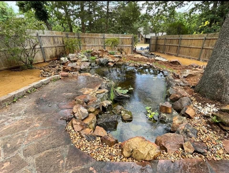 A large pond surrounded by rocks and trees in a backyard.