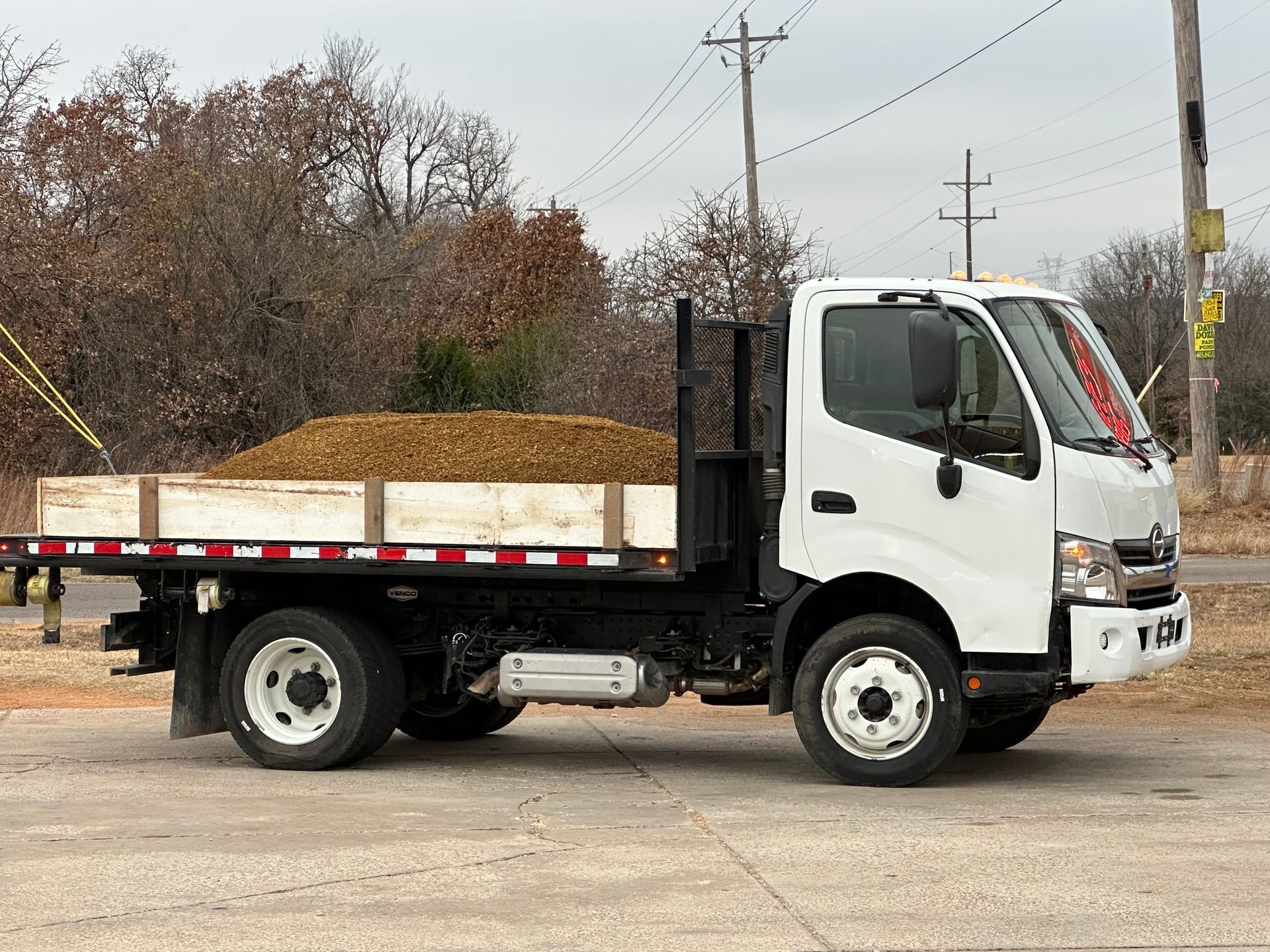 A white truck with a flat bed is parked on the side of the road.