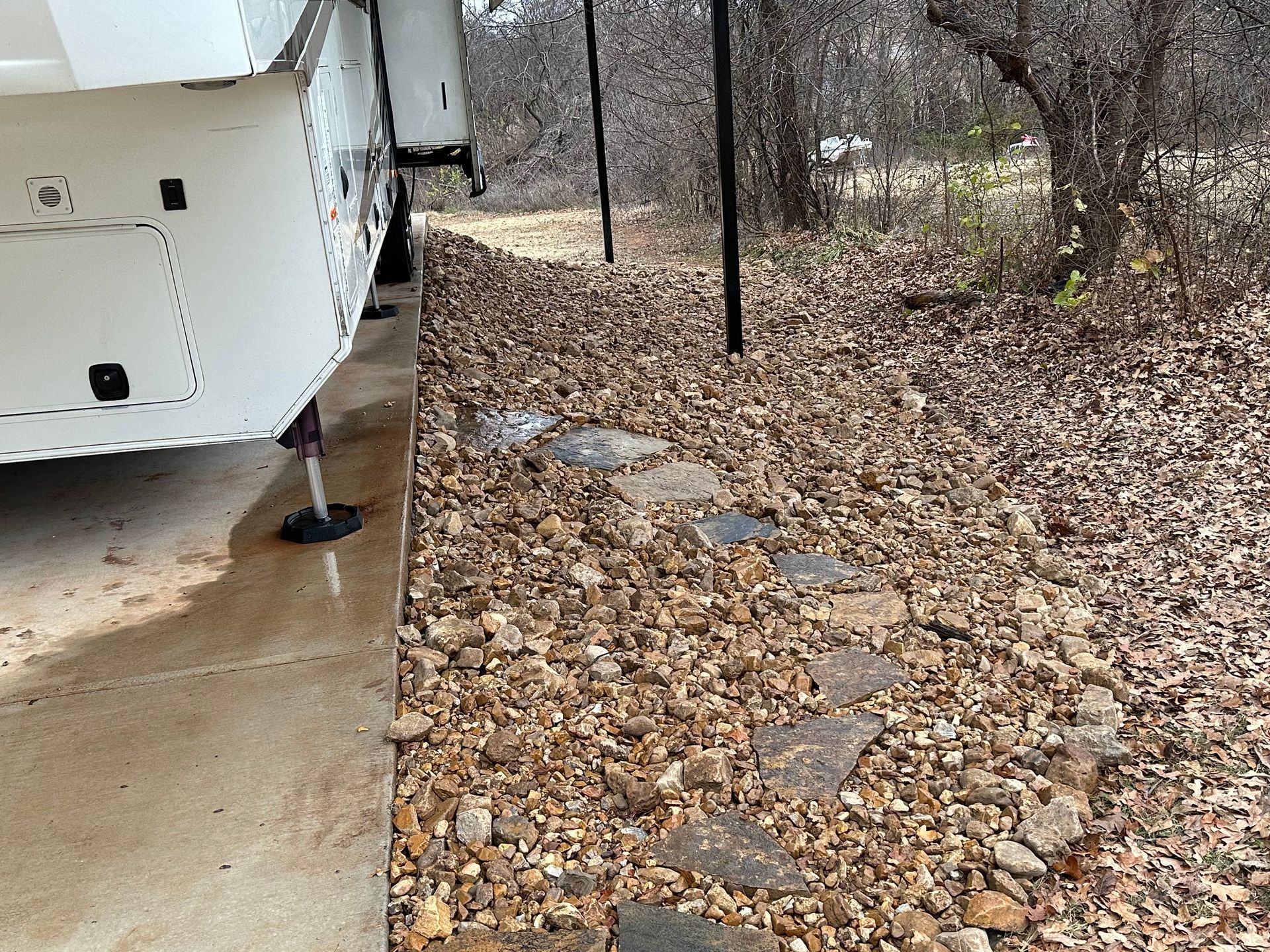 A white trailer is parked on a gravel road next to a forest.