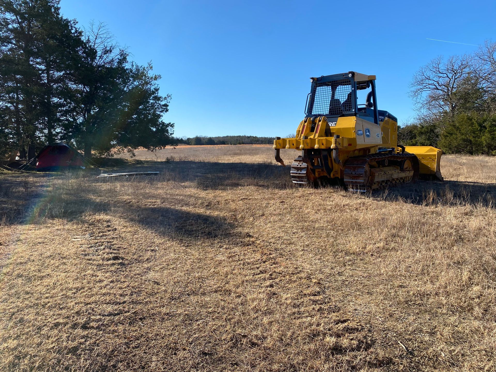 A yellow bulldozer is driving through a dry grass field.