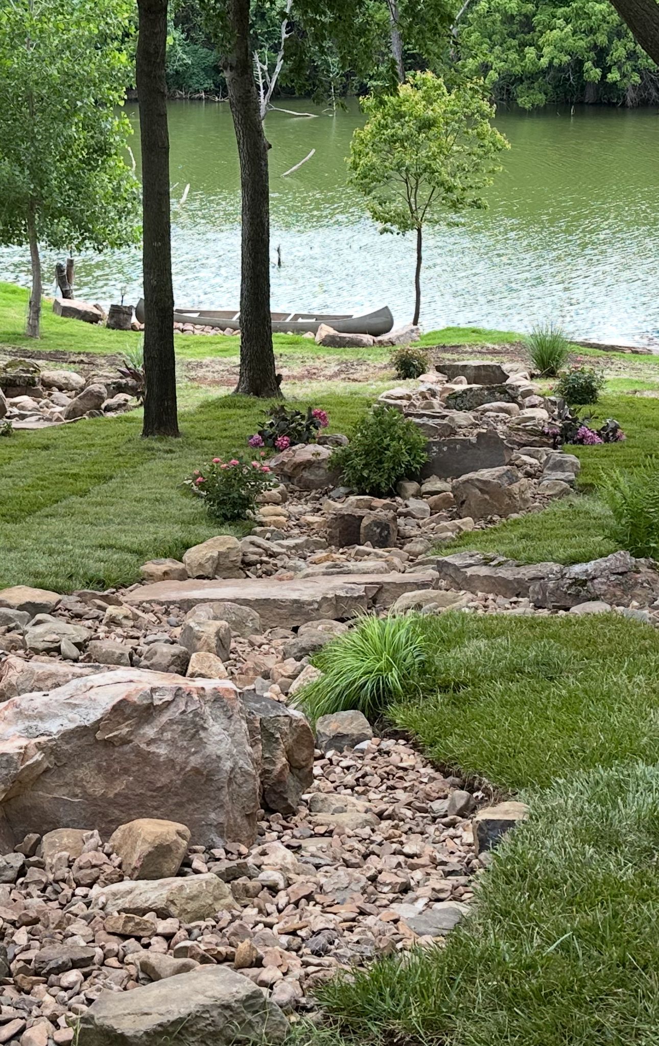 A rocky path leading to a lake surrounded by trees and grass.
