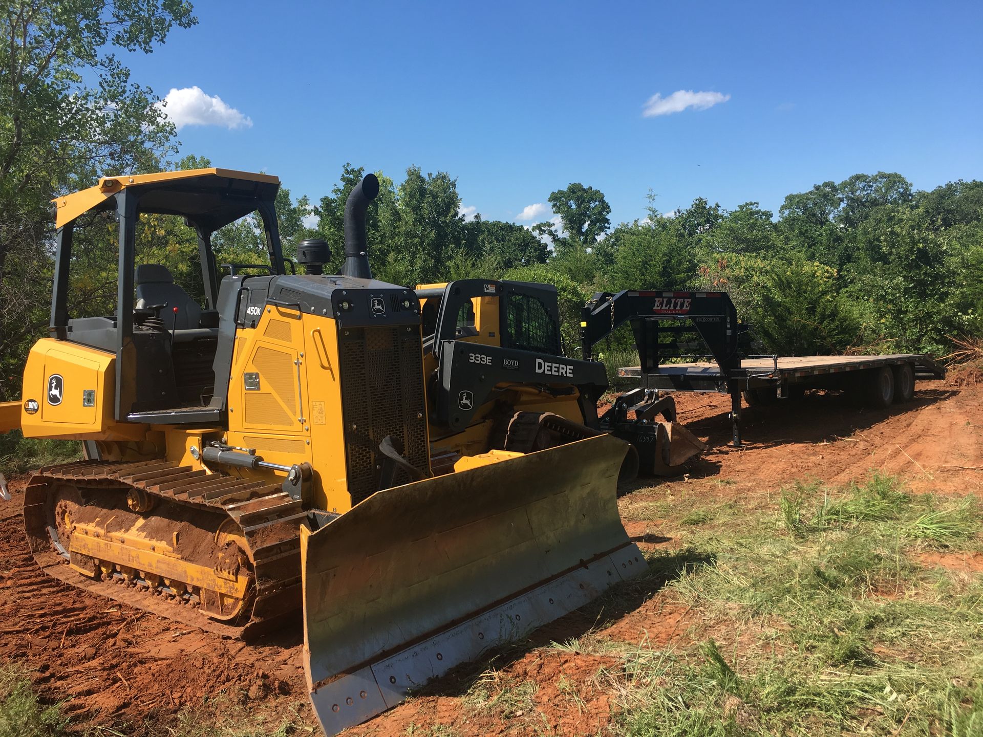 A yellow bulldozer is parked in a dirt field next to a trailer.