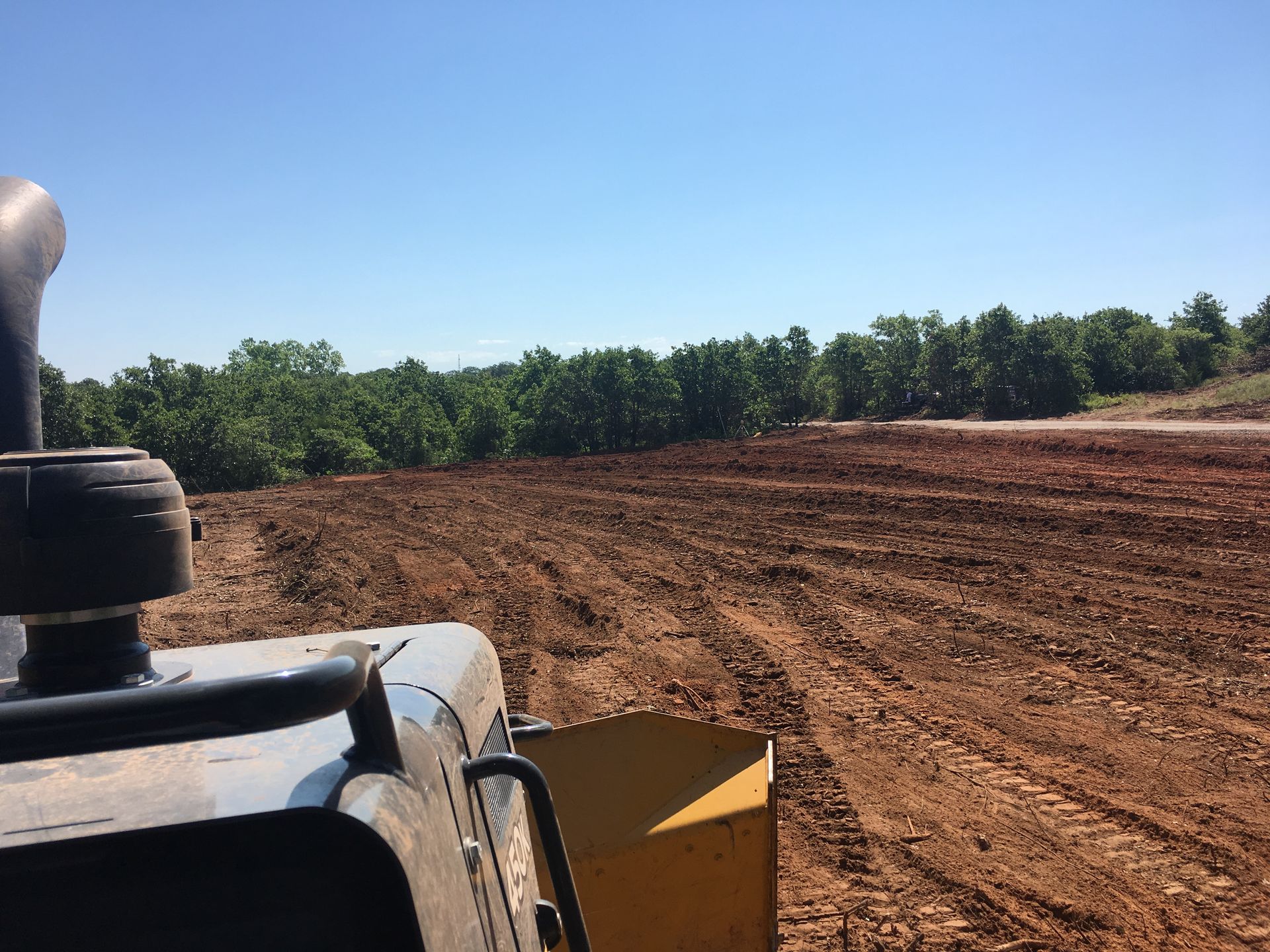 A bulldozer is plowing a dirt field with trees in the background.