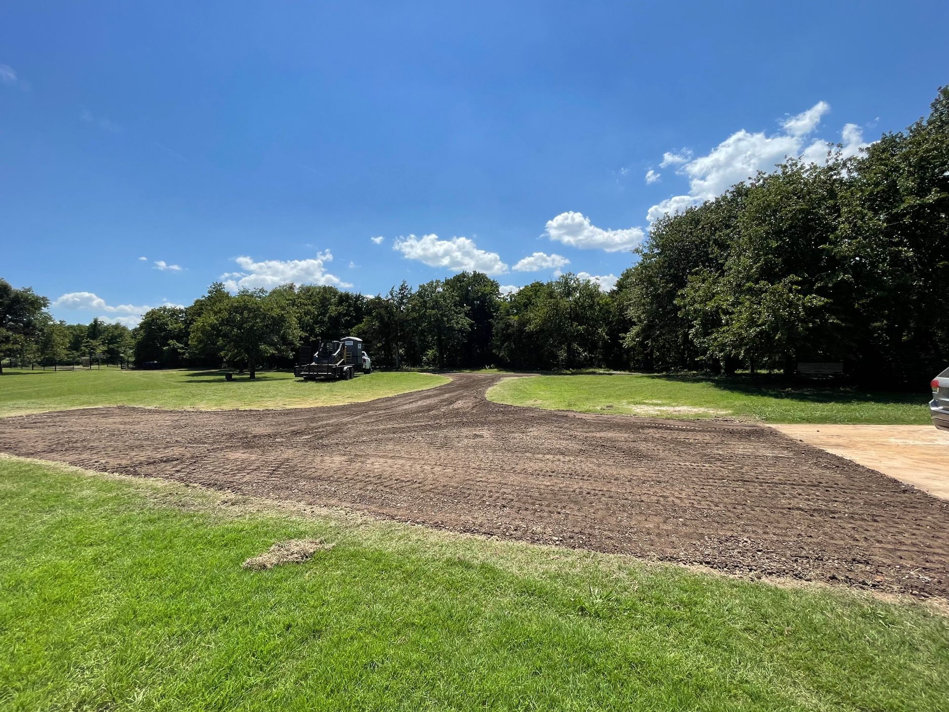A dirt road going through a grassy field with trees in the background.