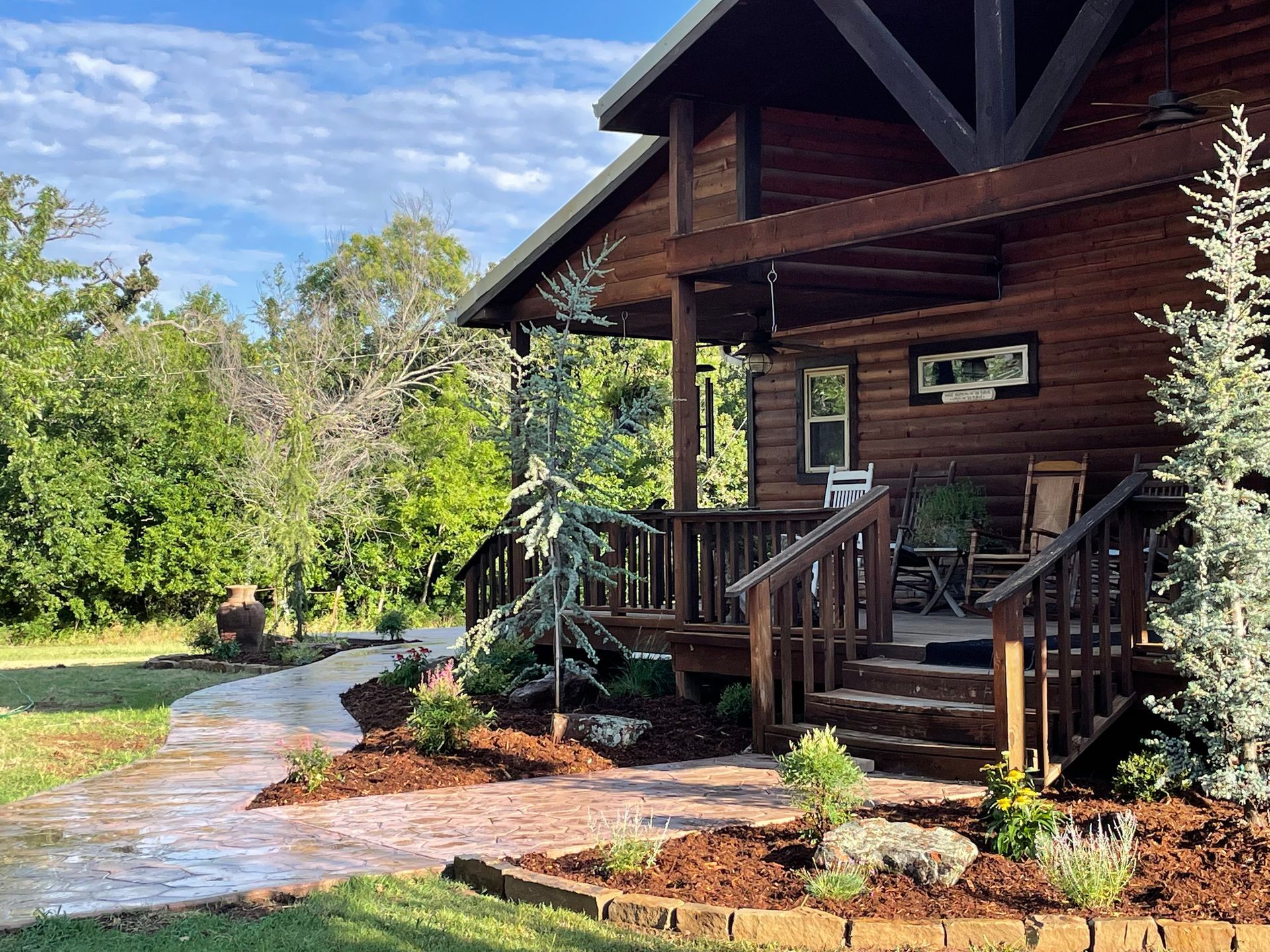 A log cabin with a porch and stairs is surrounded by trees.