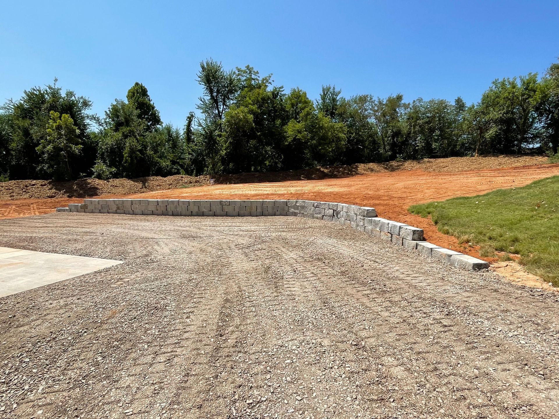 A gravel driveway with a stone wall and trees in the background