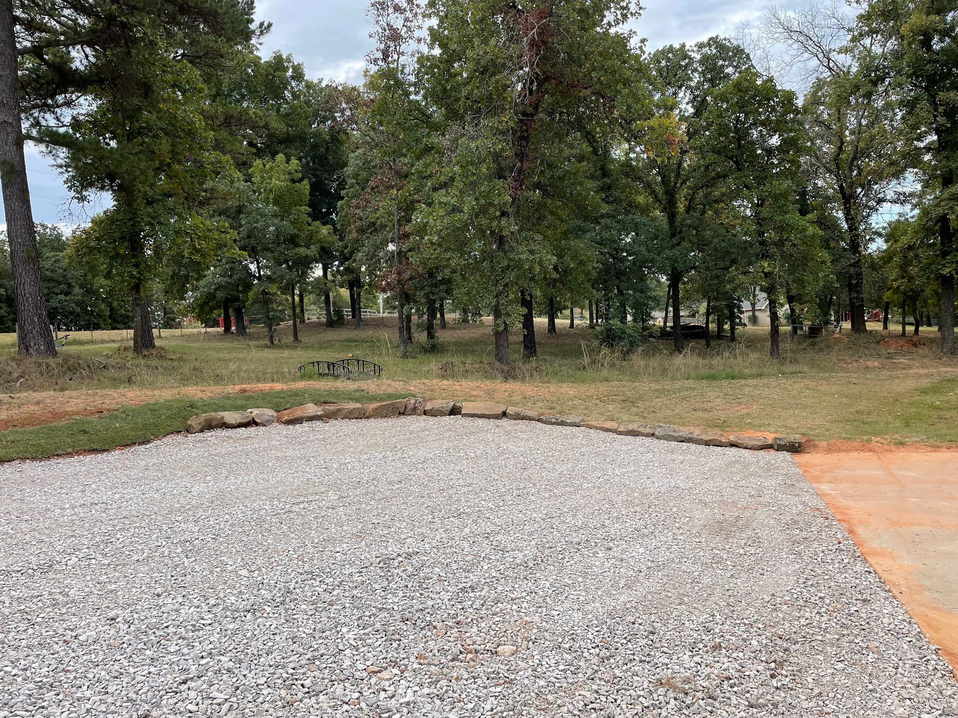 There is a gravel driveway in the middle of a field with trees in the background.