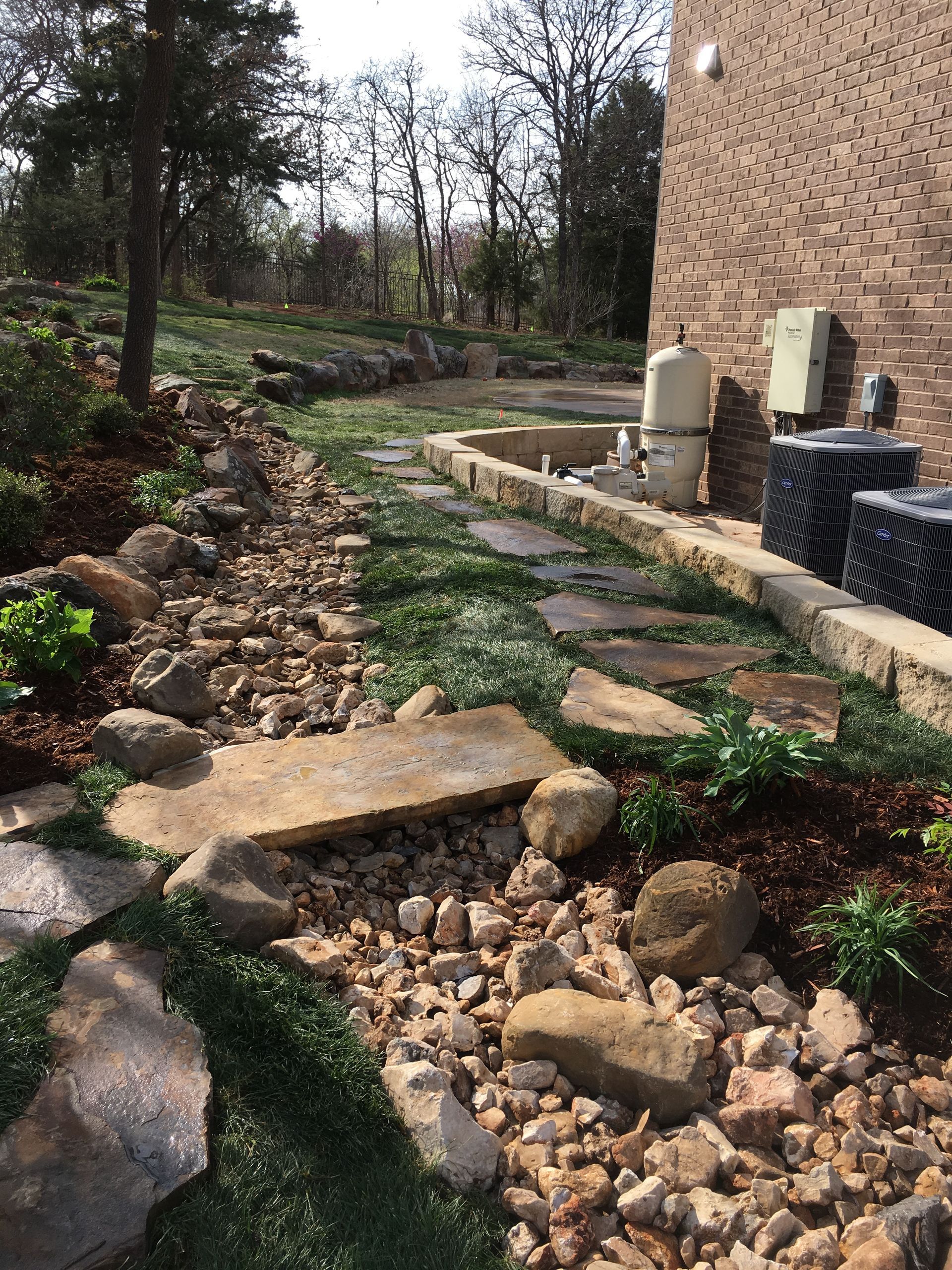 A stone walkway leading to a house with a brick building in the background.