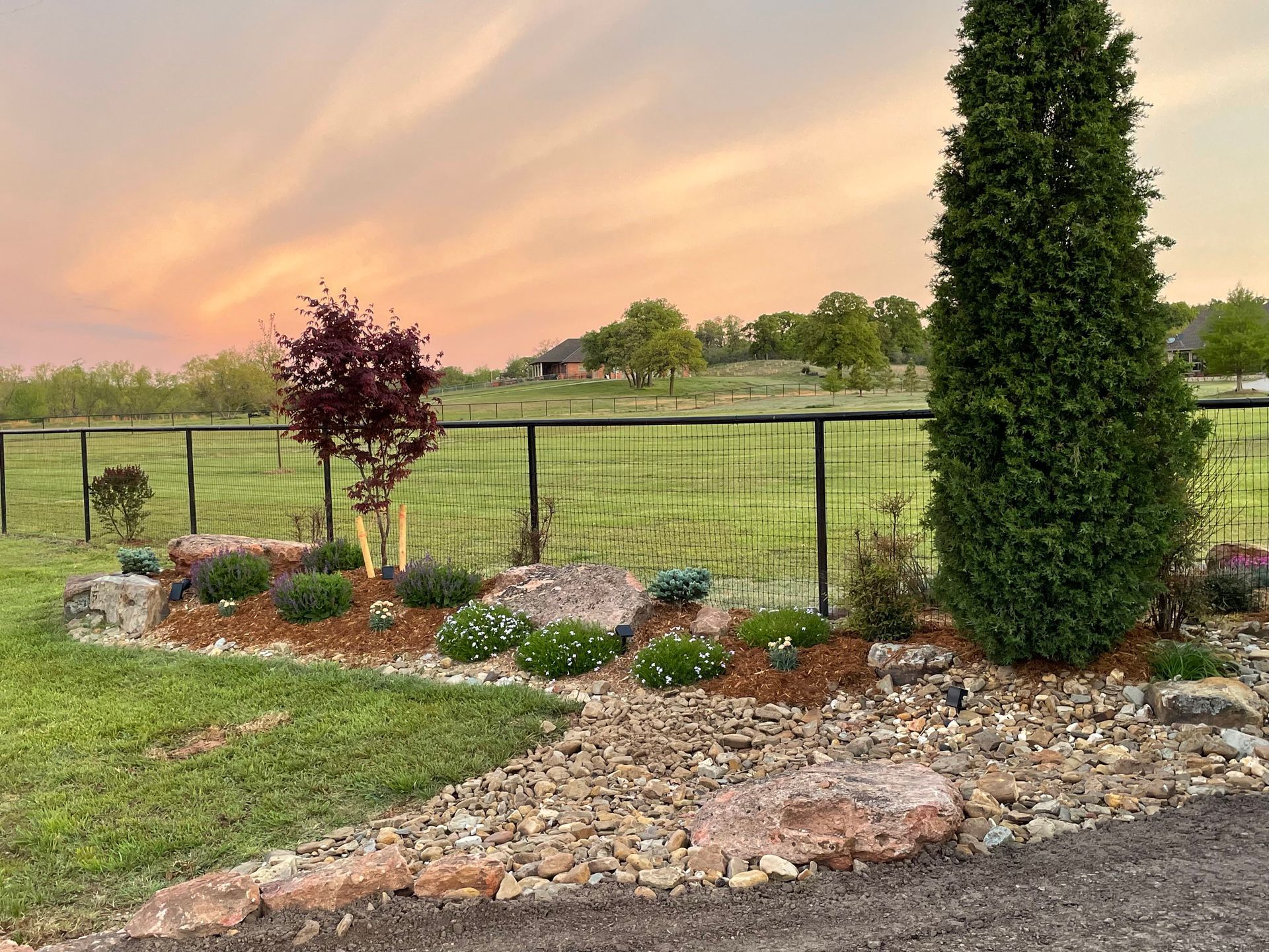 A fence surrounds a lush green field with a sunset in the background.