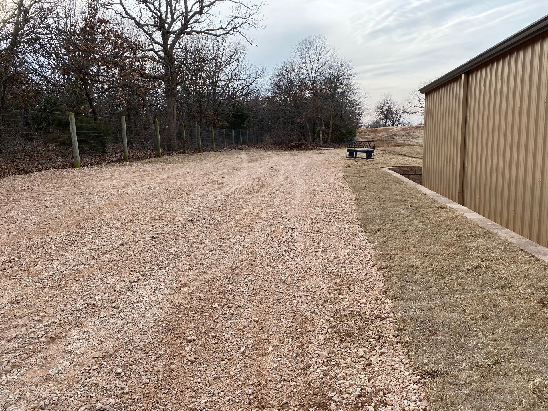 A gravel road leading to a building with trees in the background.