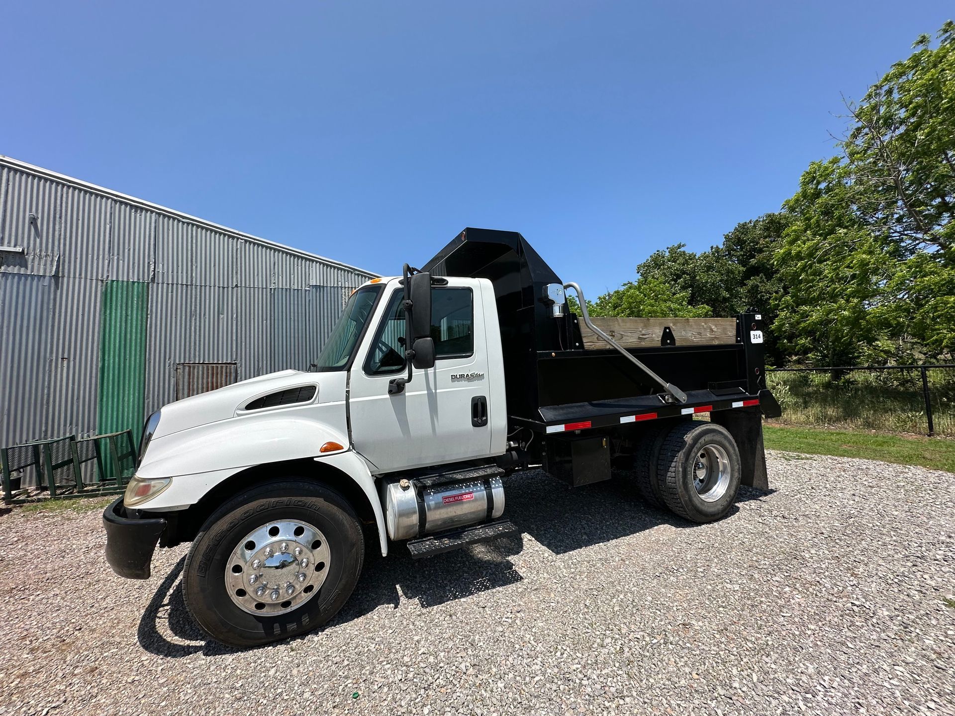 A white dump truck is parked in a gravel lot in front of a building.