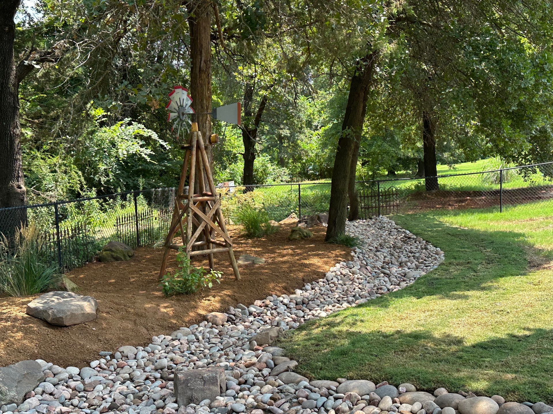 A windmill is sitting in the middle of a lush green field next to a stream of rocks.