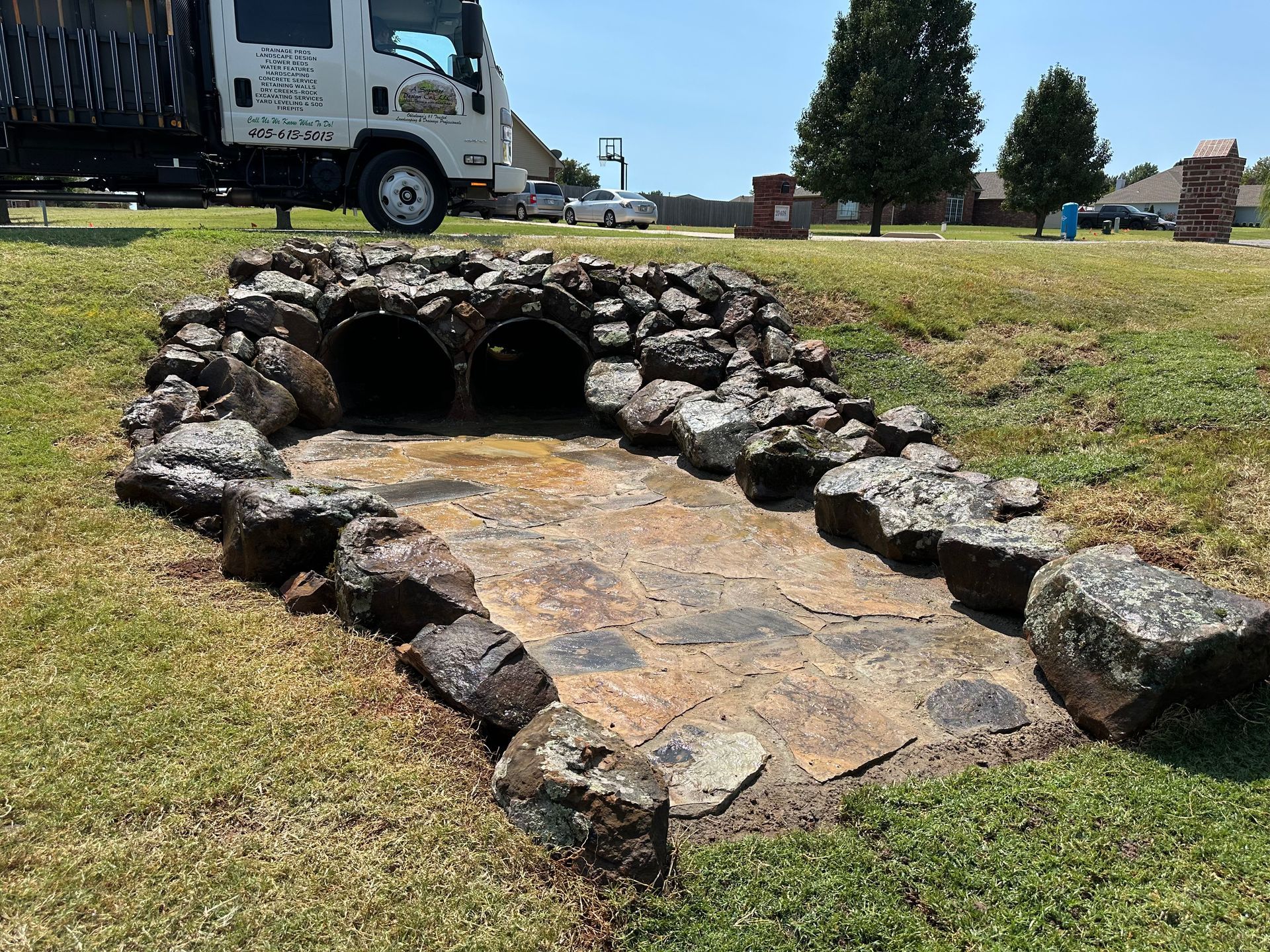 A truck is parked next to a stone bridge in a grassy field.