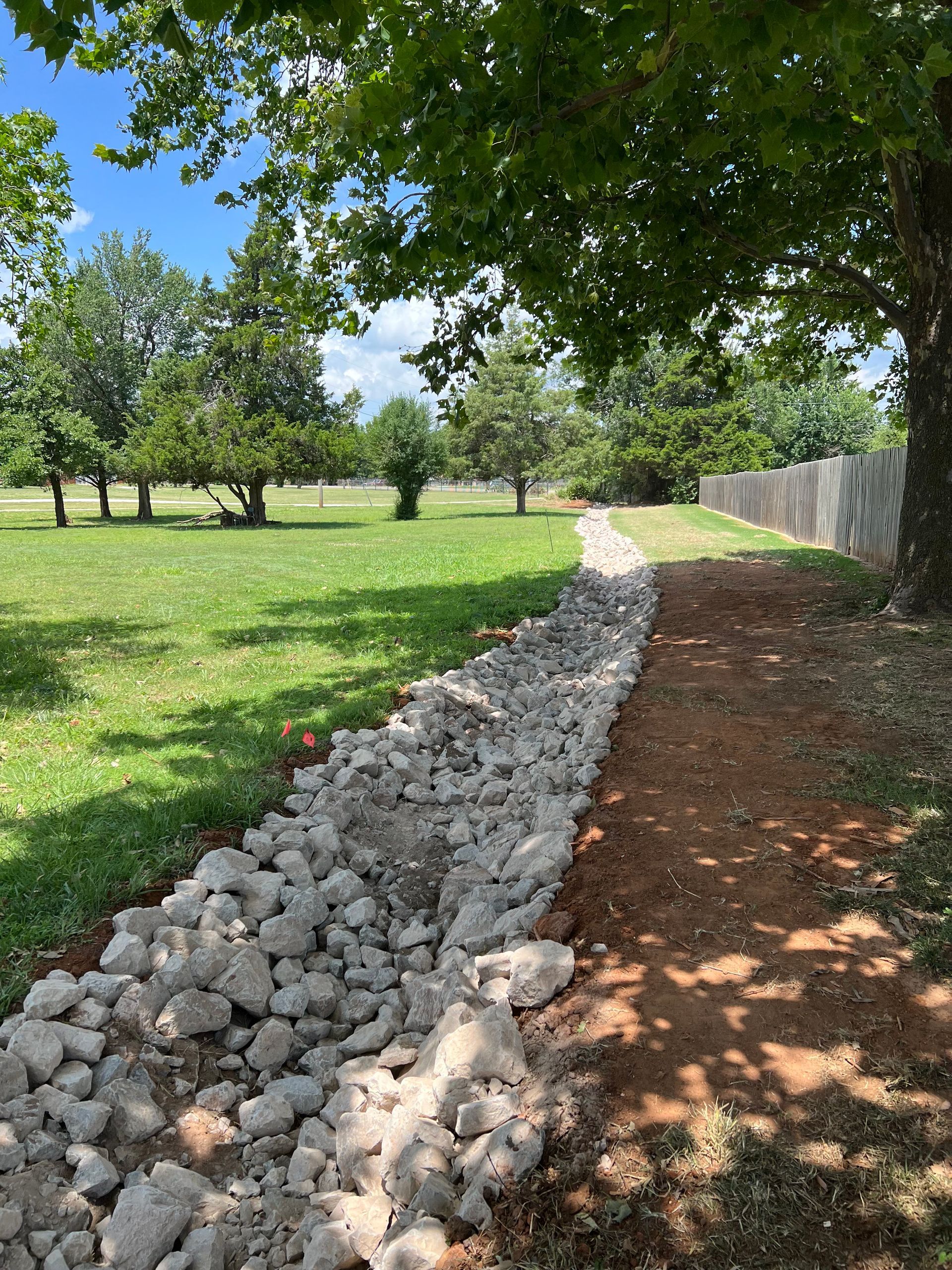 A dirt path surrounded by rocks leading to a grassy field.